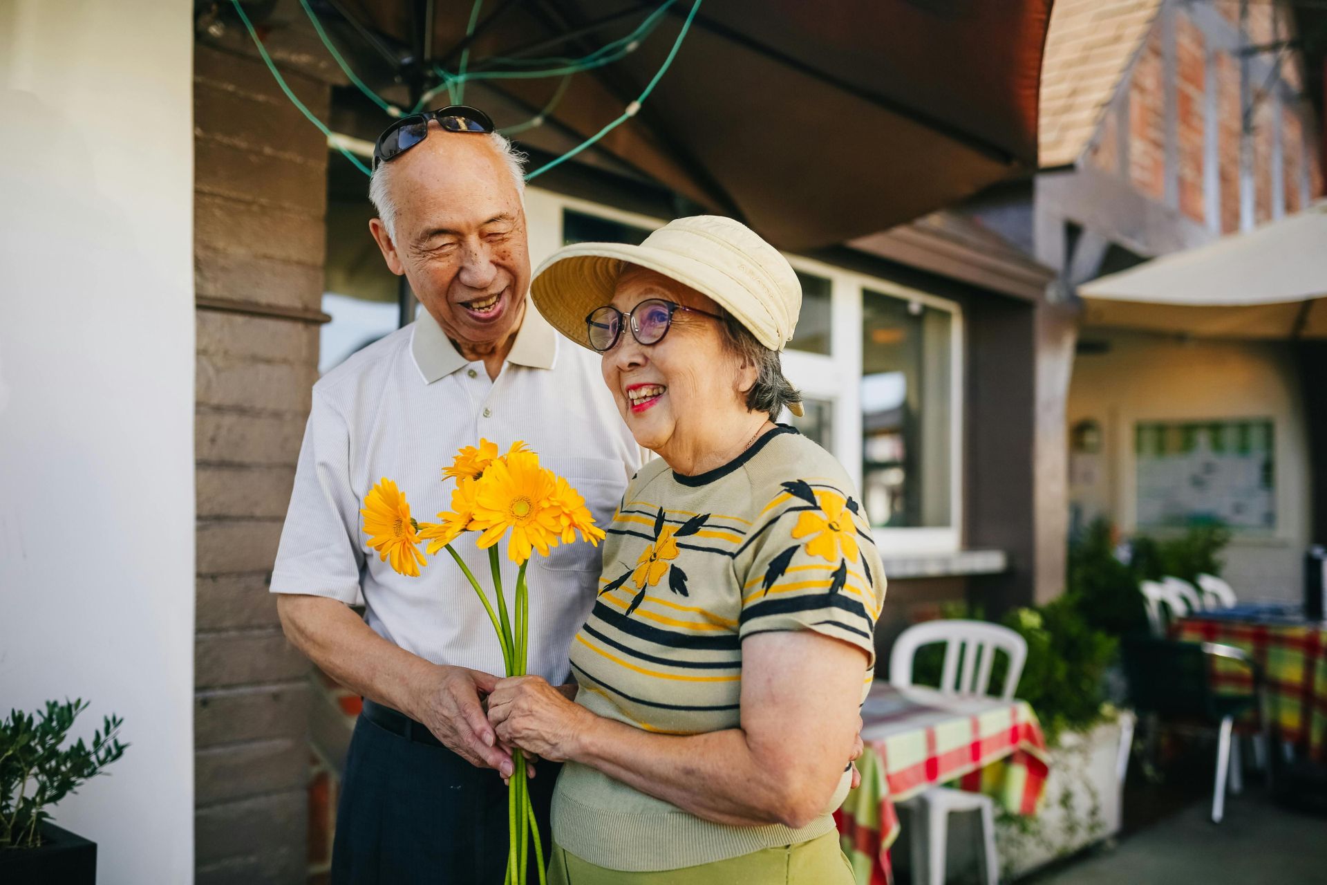 Happy senior couple enjoying a moment with yellow flowers outside a restaurant.