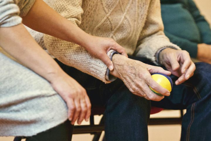 An elderly person receives support from a caregiver, holding hands indoors, showcasing compassion.